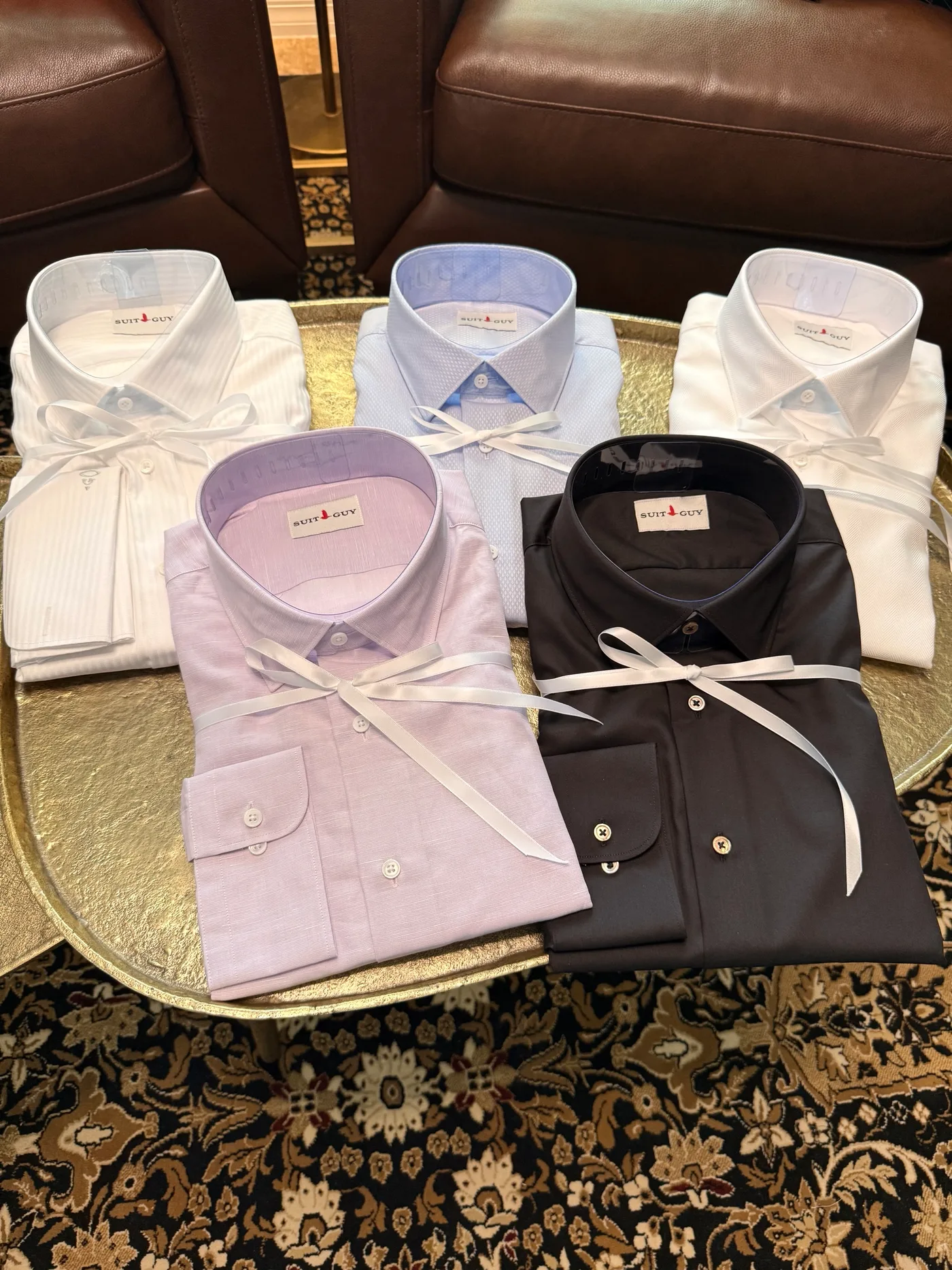 Five custom shirts folded and tied with white ribbon on a gold tray