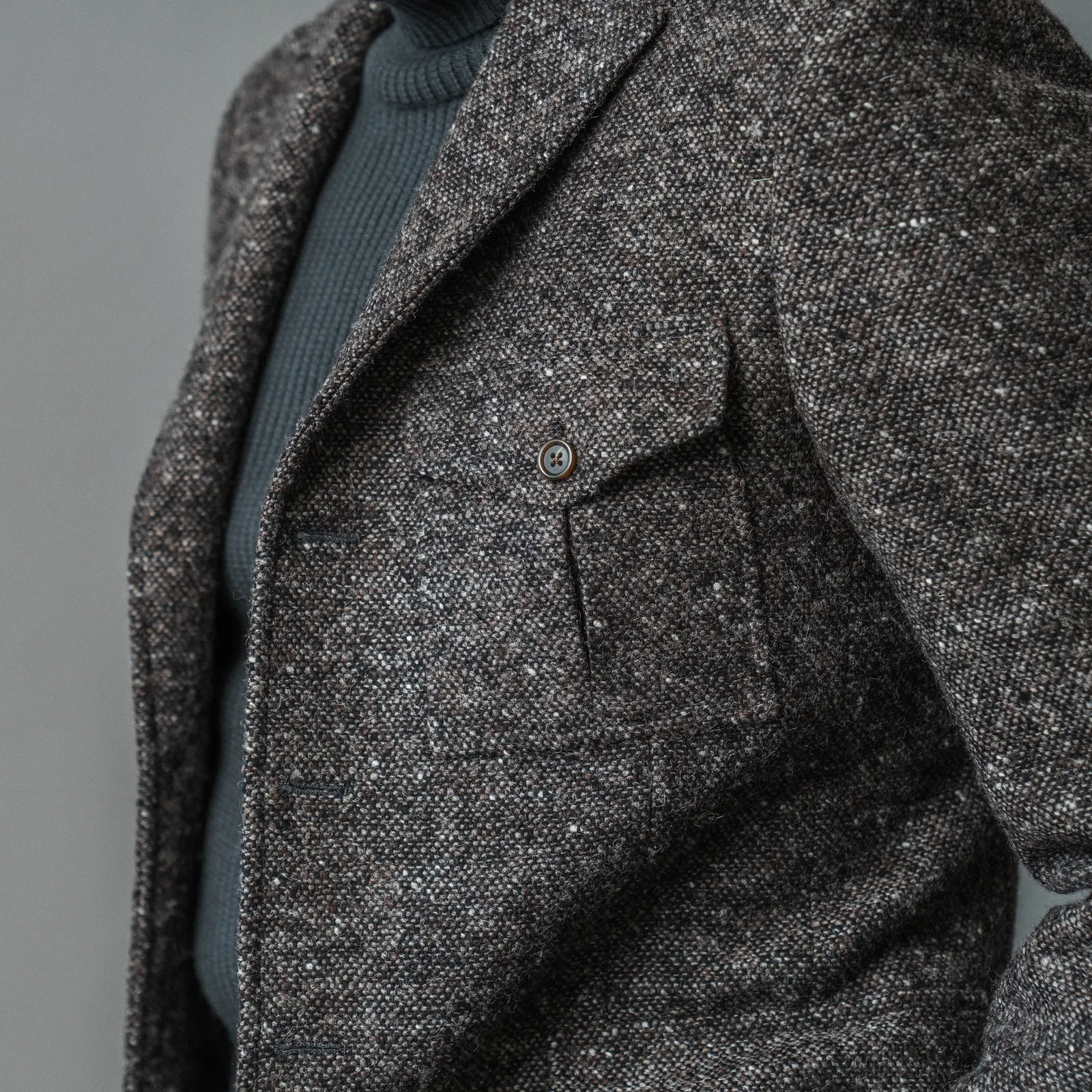 Close view of a charcoal tweed jacket with a flap pocket