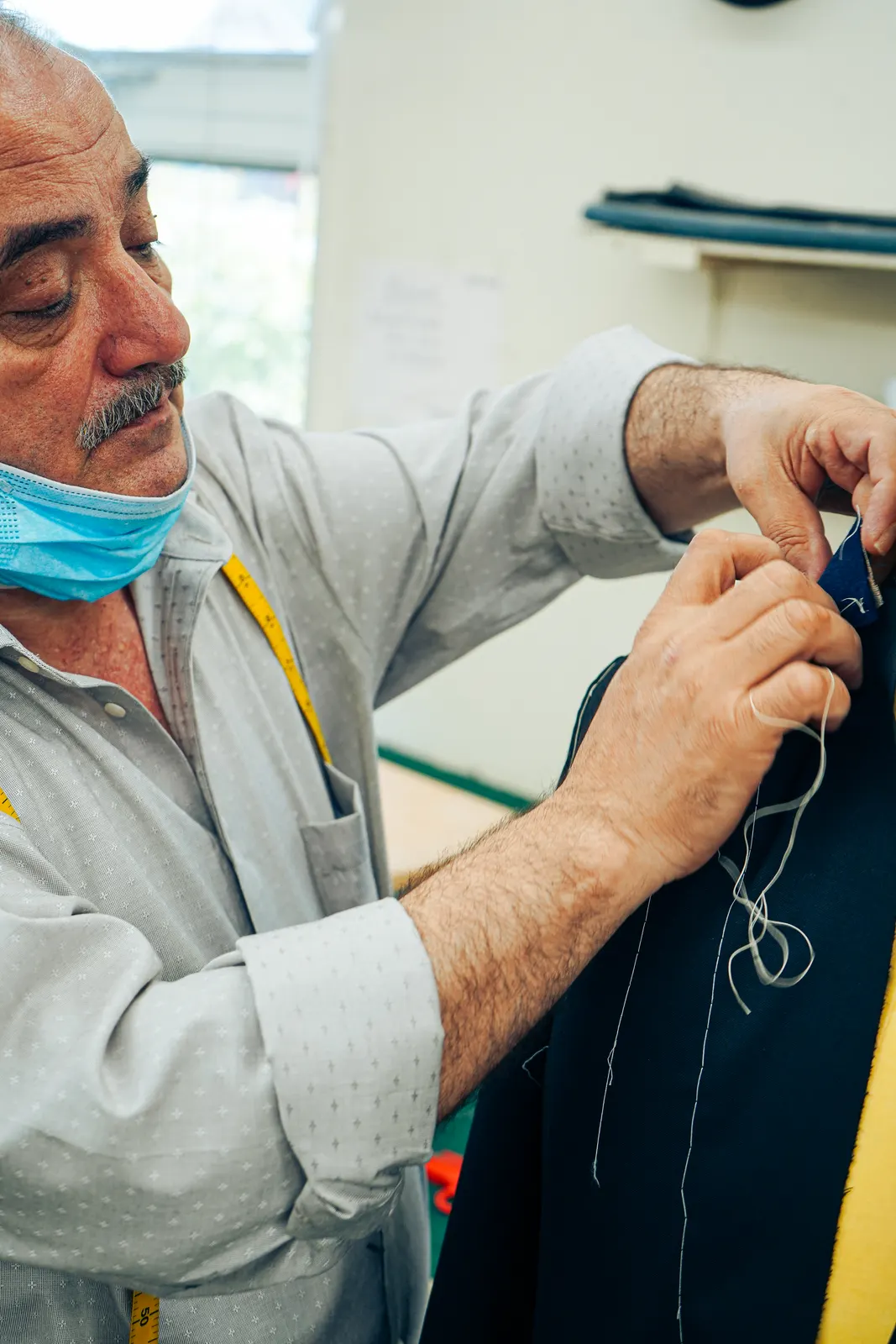 A tailor hand-stitching a navy jacket