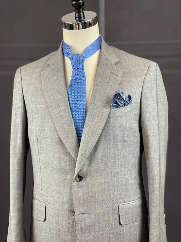 A gray custom jacket on a form, with a knit tie and pocket square