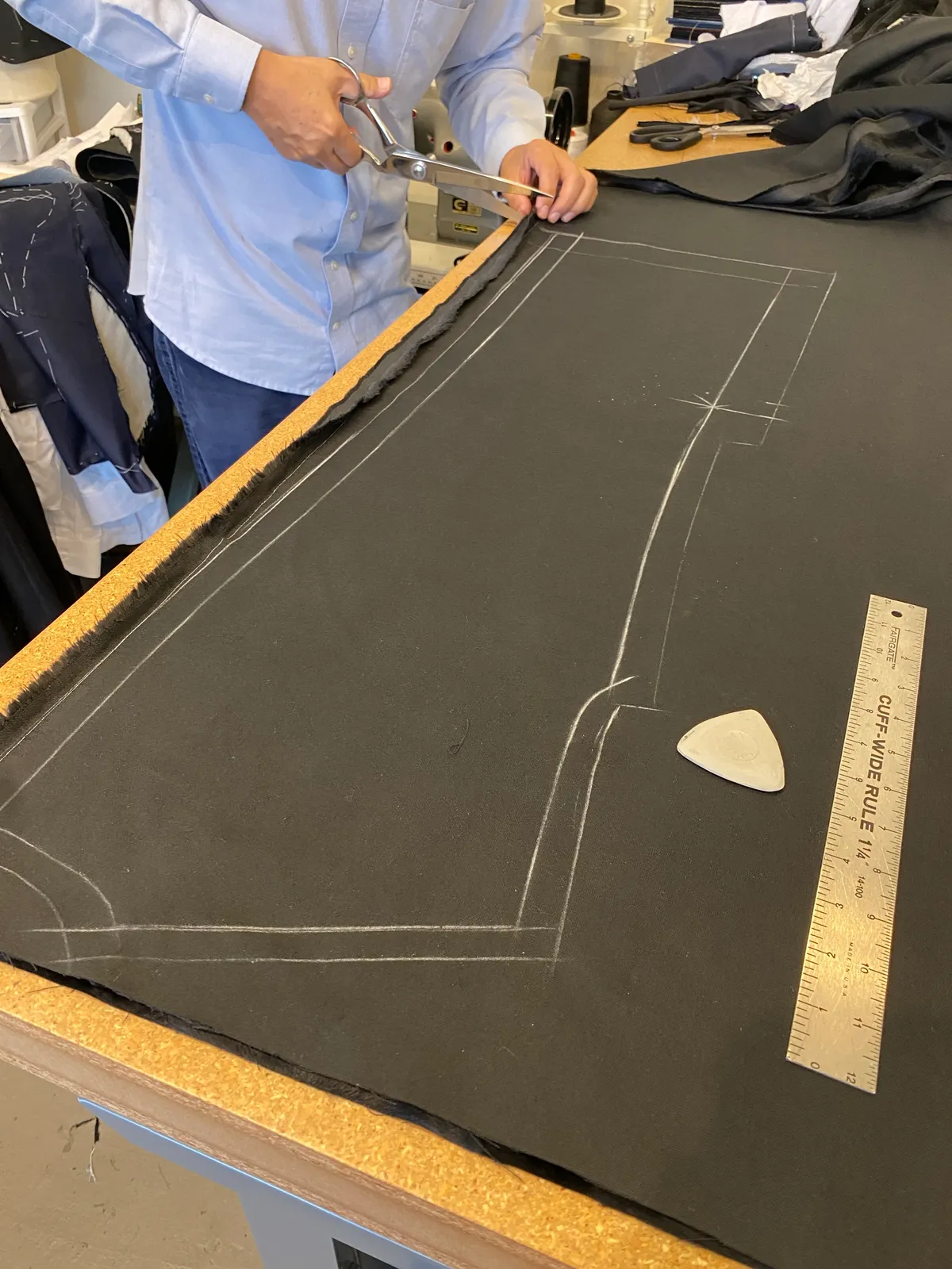 A tailor cutting along a chalked line on dark cloth