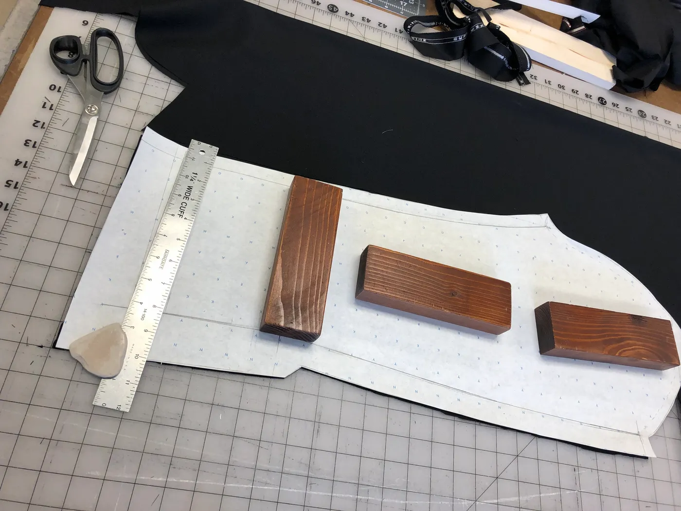 A sleeve pattern weighted with wooden blocks on black cloth before cutting