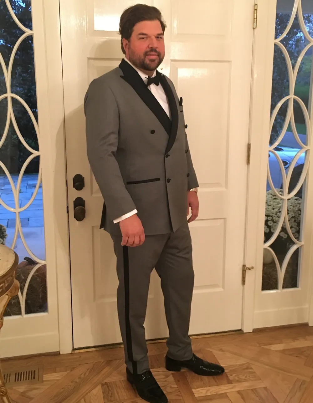 A man in a custom grey double-breasted tuxedo with black satin lapels and a side stripe on the trousers