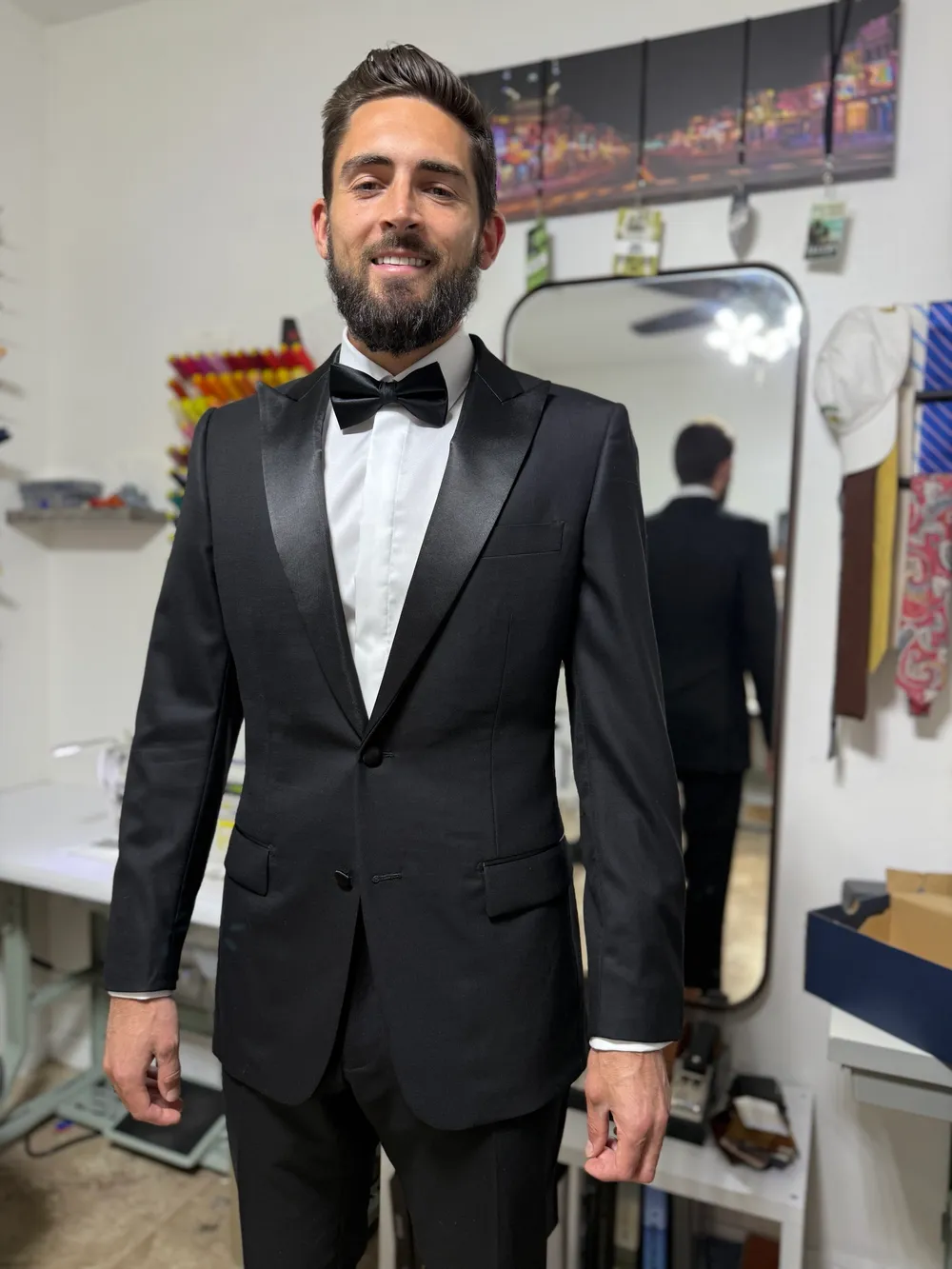 A man in a custom black tuxedo with wide satin peak lapels and a black bow tie