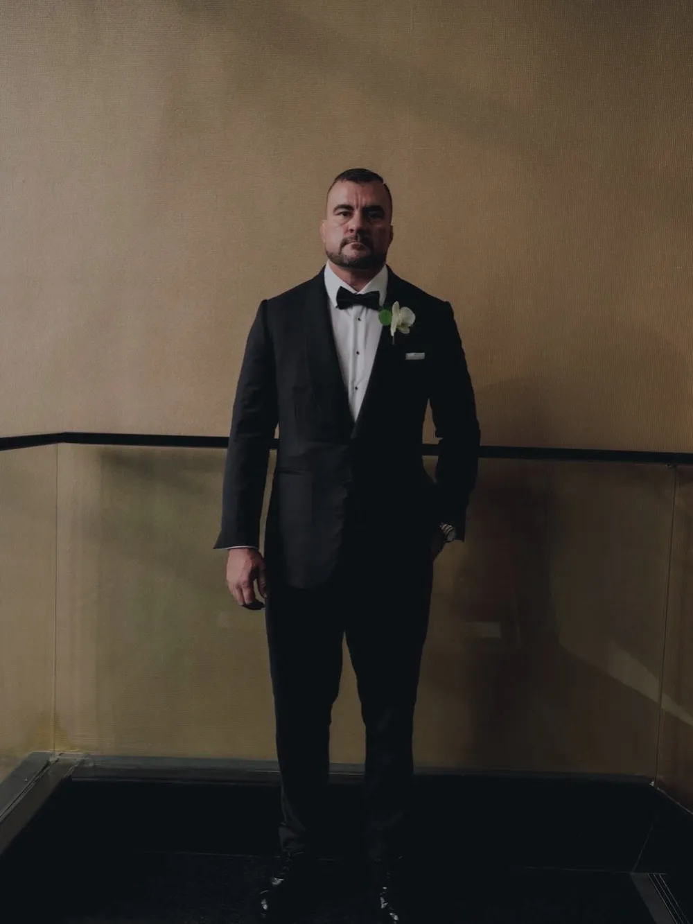 A groom in a custom black shawl-collar tuxedo with a white orchid boutonniere