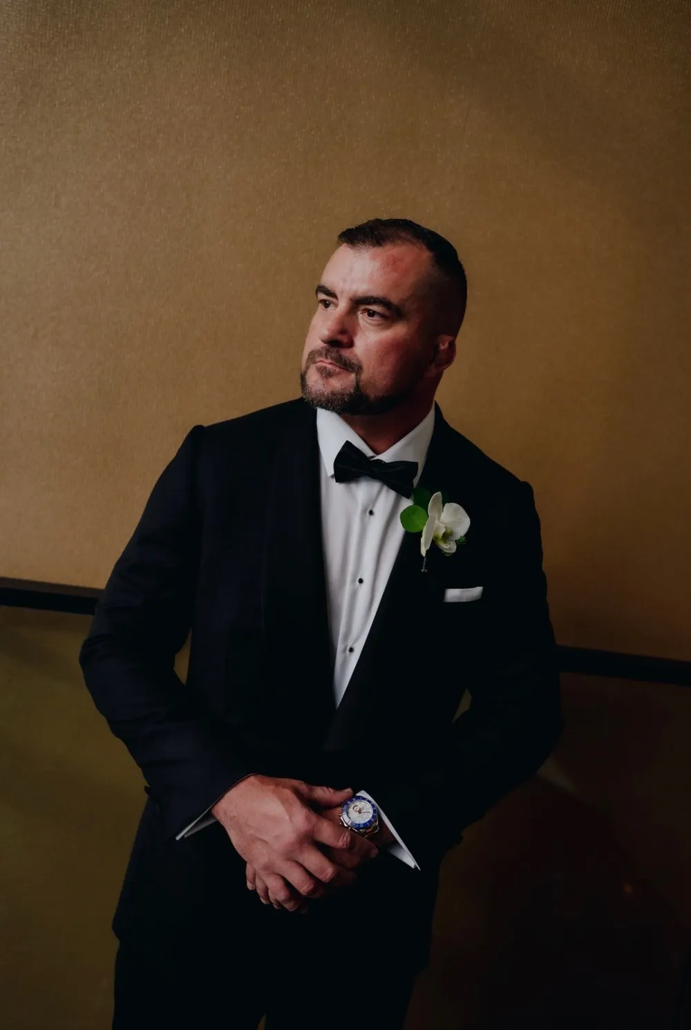A close portrait of a groom in a custom shawl-collar tuxedo with a white orchid and watch