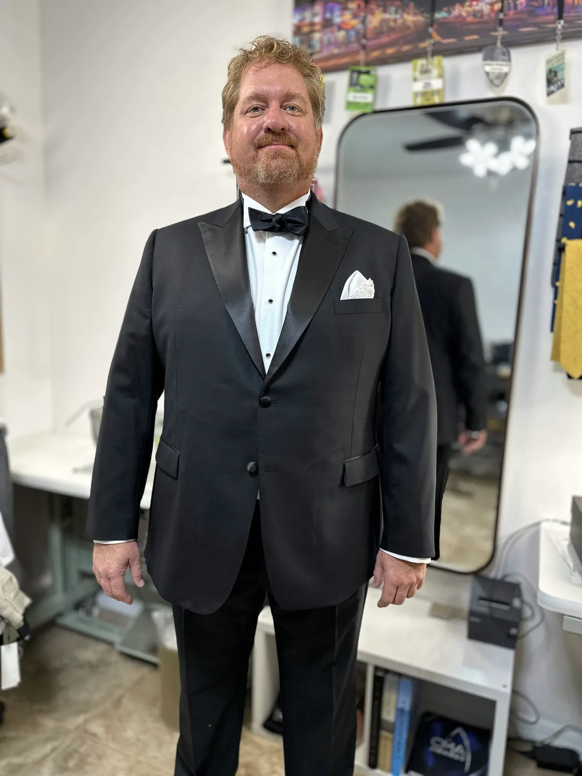 A groom in a custom black tuxedo with a satin peak lapel, white pique shirt, bow tie and white pocket square