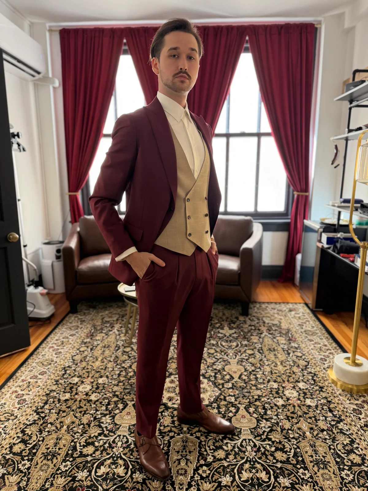 A groom in a custom burgundy three-piece suit with a tan double-breasted vest and brown monk-strap shoes