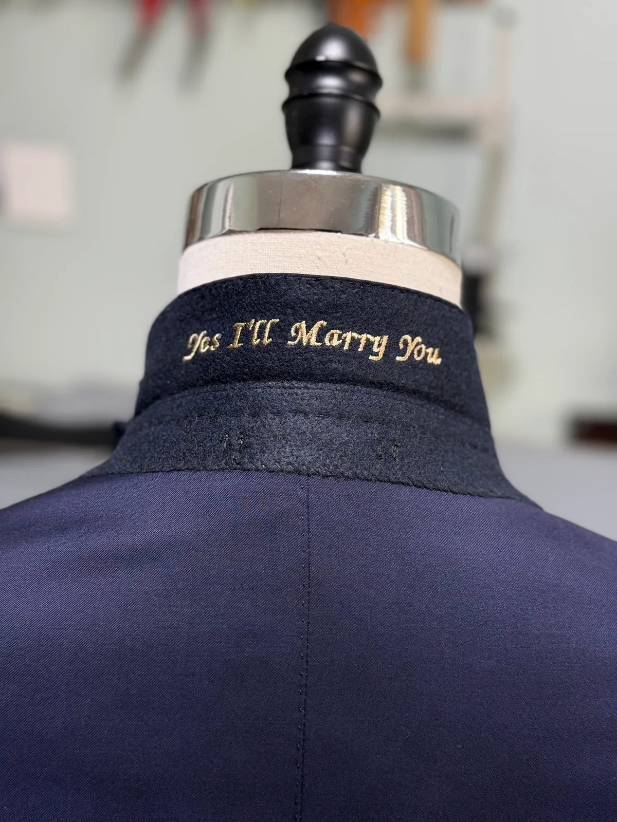 The inside collar of a navy jacket embroidered in gold with the words Yes I'll Marry You
