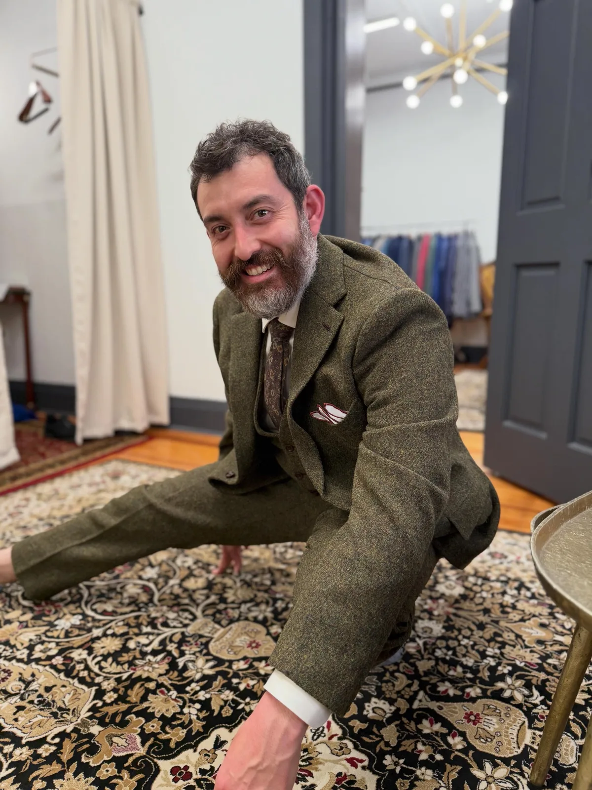 A groom in a custom olive tweed three-piece suit crouching low to show how freely the suit moves