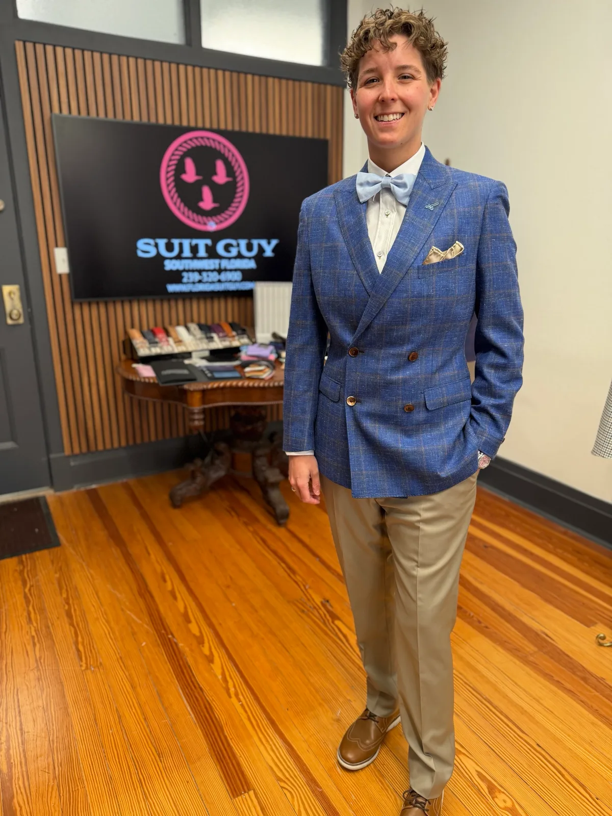 A woman in a custom blue double-breasted blazer with tan trousers, a light blue bow tie and a gold pocket square